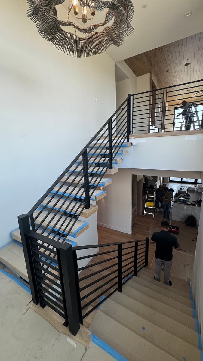 Black horizontal-bar handrail section on a staircase and upper landing while the house is being finished