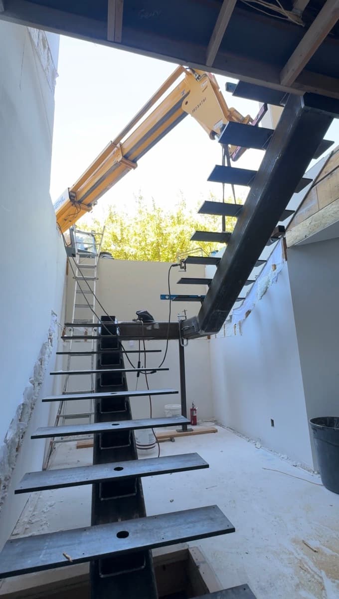 Single-spine steel stair with plate treads in a light well, a telehandler boom above