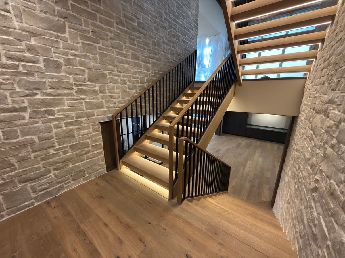 Finished open-riser staircase with black steel pickets between two stone walls
