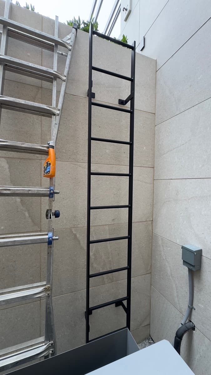 Black steel access ladder mounted to a tiled exterior wall
