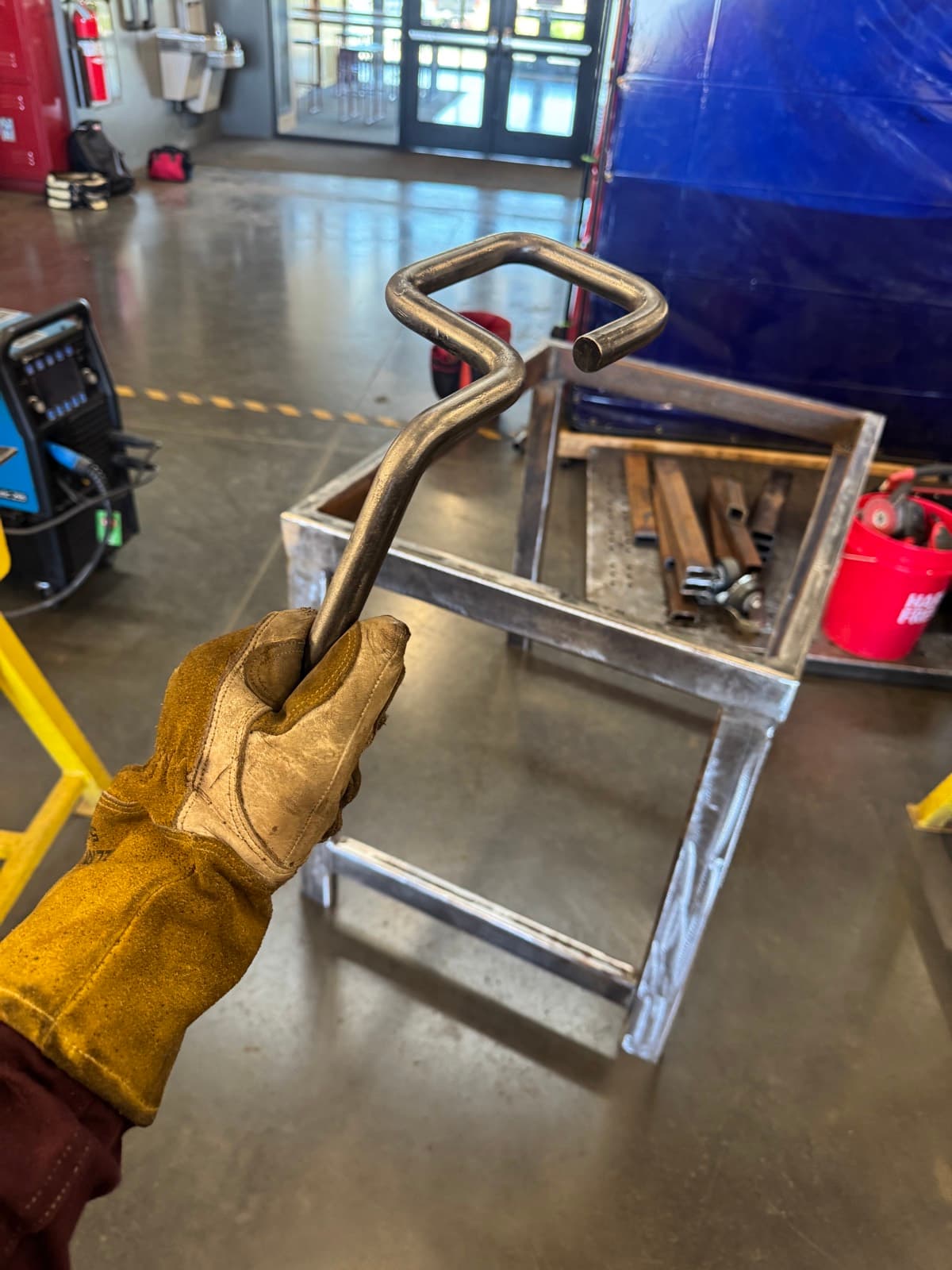 Holder bent from solid bar for an arc gouger, in front of a welded arc gouging table